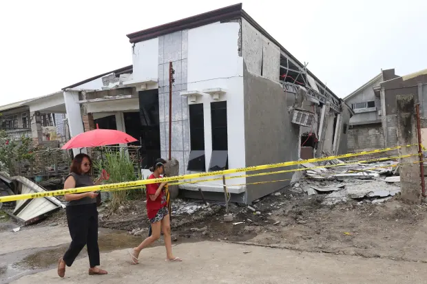 Two women walk past a damaged house after a strong...