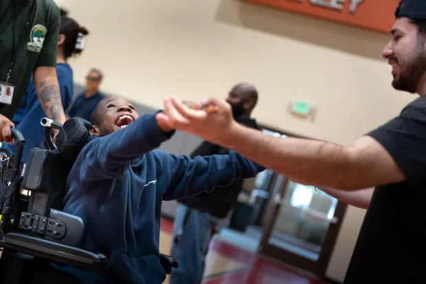 Jacob Pinedo, therapist, right, works with Xavier Young in gym...