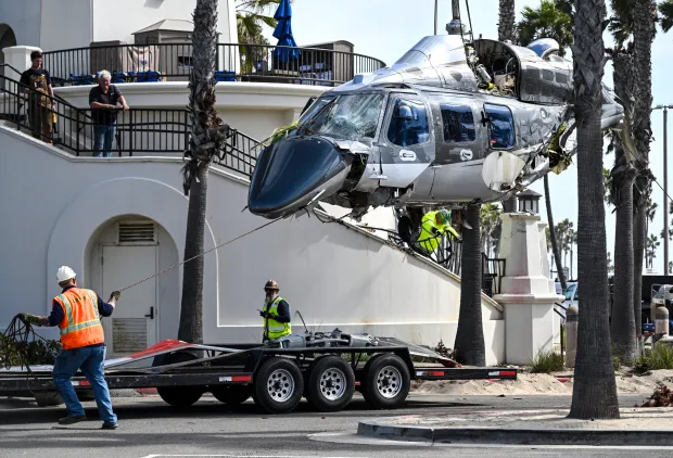 Workers use a crane to remove a 1980 Bell 222...